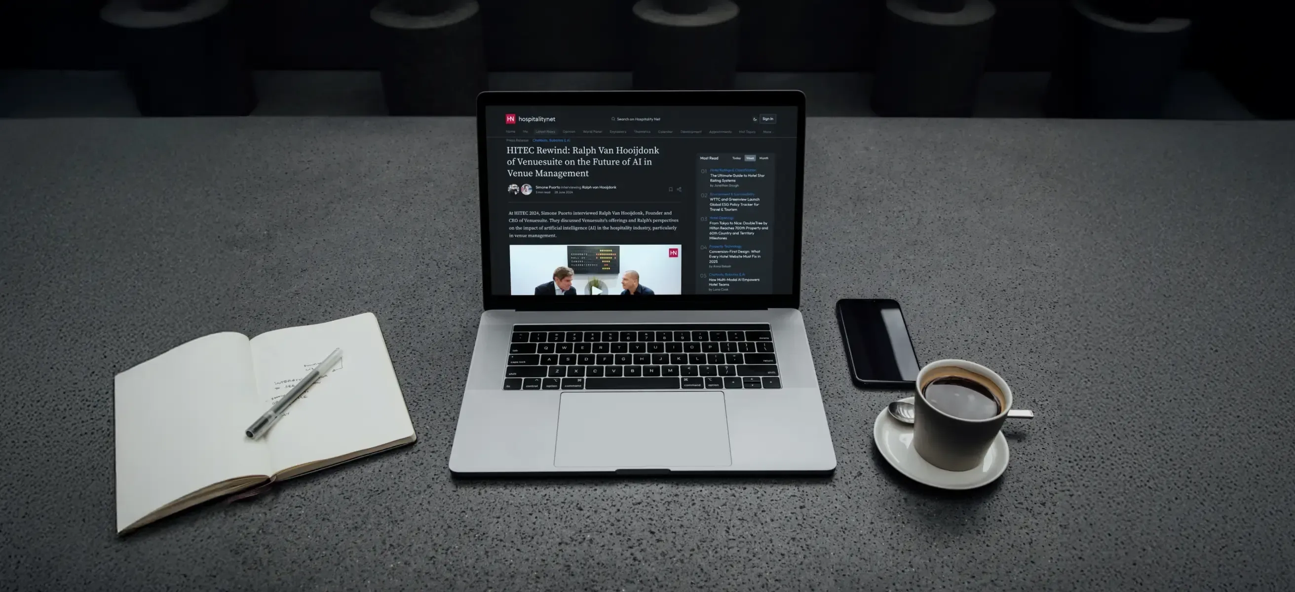 Afbeelding van een tafel met een laptop waar de webpagina van de Hospitality.net blog over AI in hospitality op staat weergegeven, kop koffie en open notitieboek.