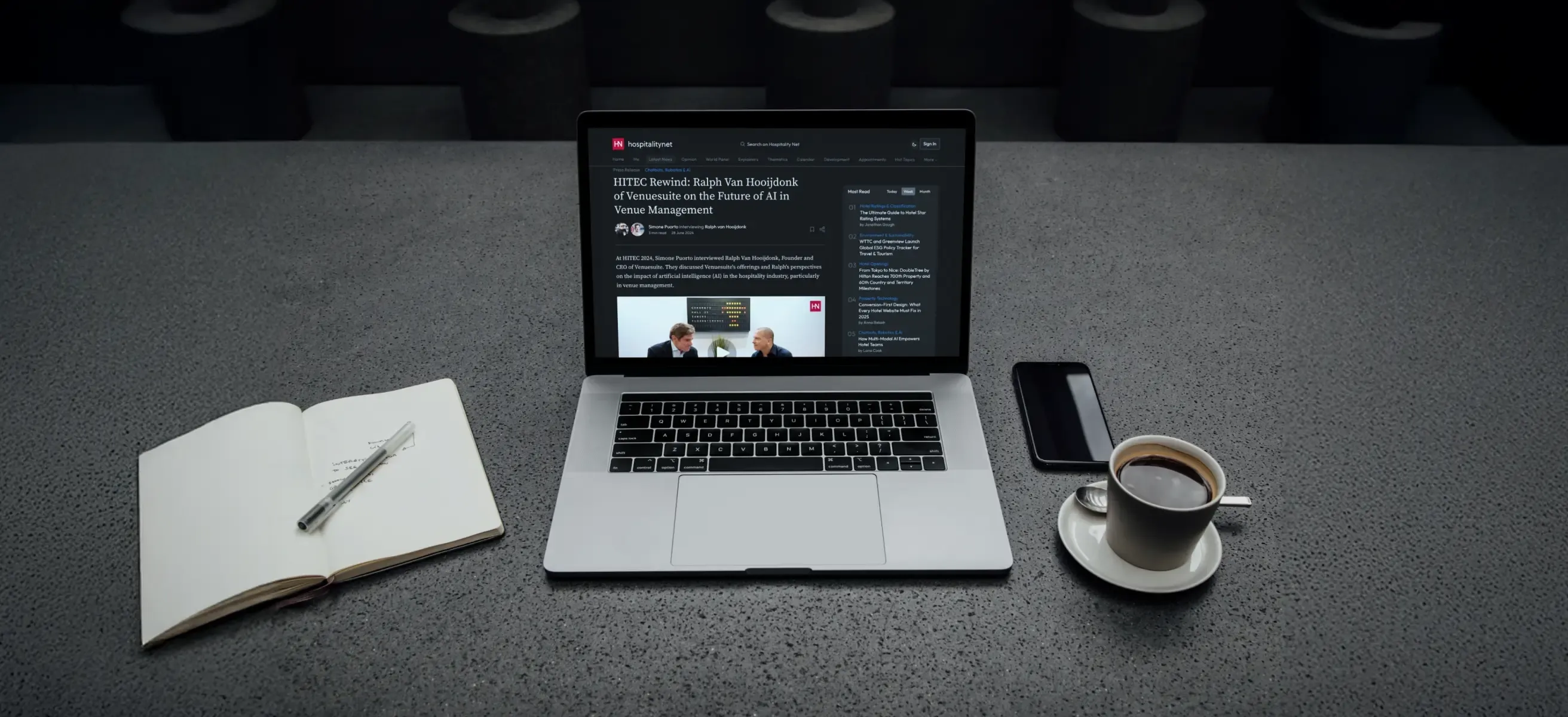 Afbeelding van een tafel met een laptop waar de webpagina van de Hospitality.net blog over AI in hospitality op staat weergegeven, kop koffie en open notitieboek.