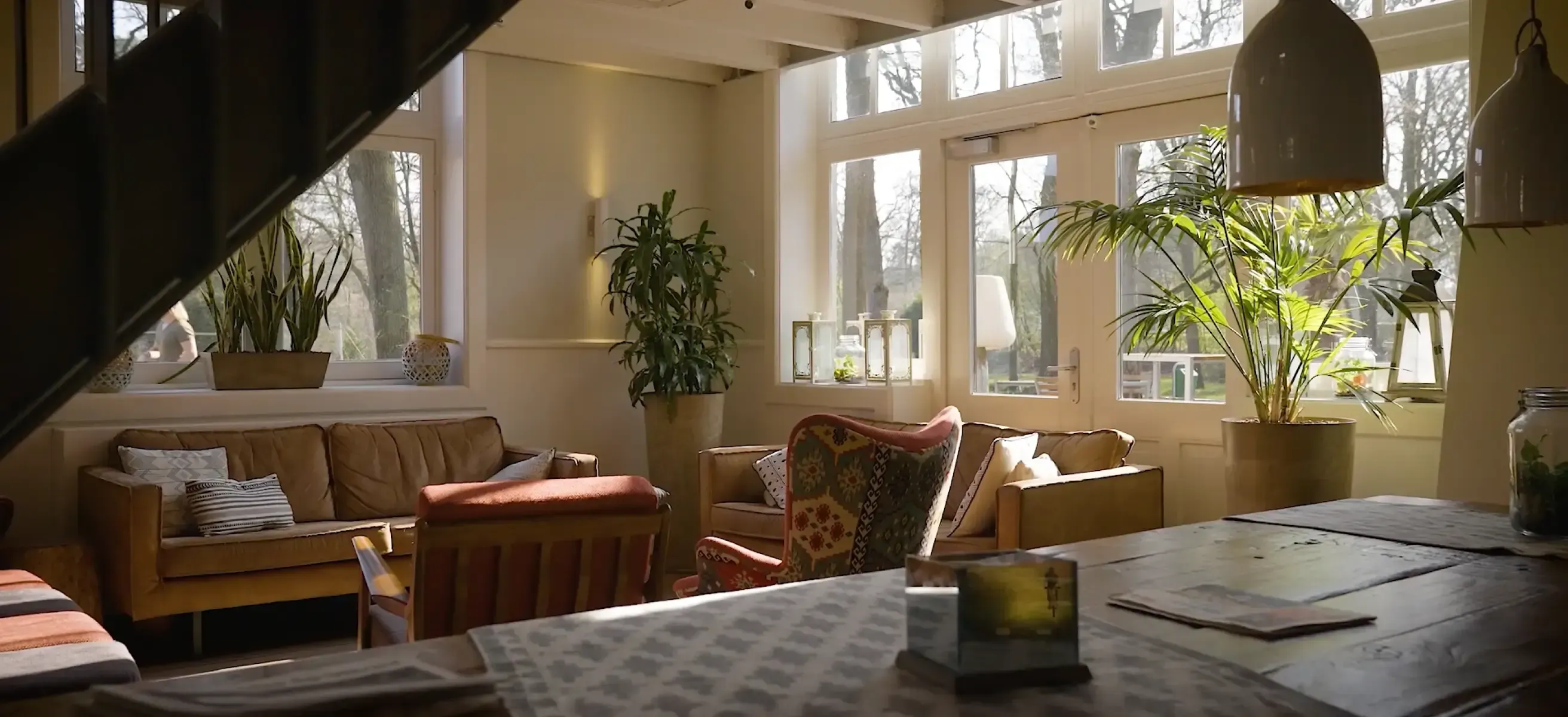 a stayokay hostels lounge area with cozy chairs, a wooden table and soft lighting.